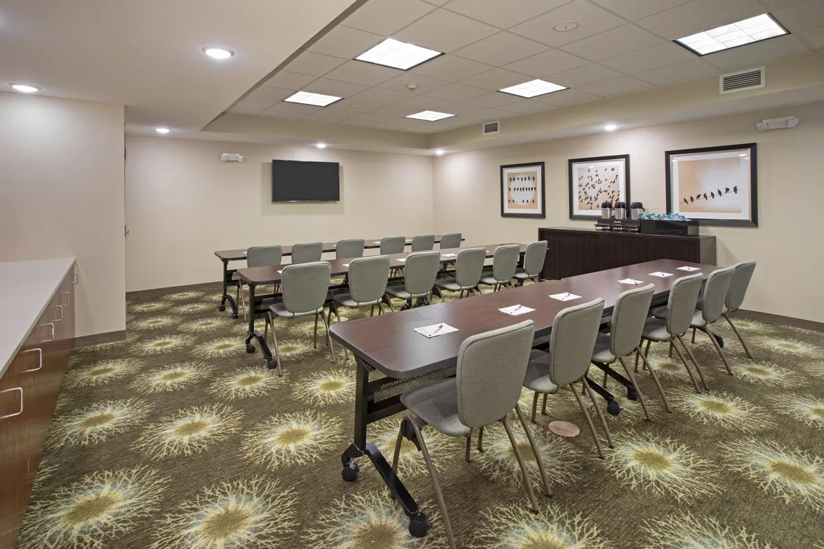 An interior meeting space featuring a long conference table with ergonomic chairs, a wall-mounted TV for presentations, and decorative artwork. The room is designed for productivity, collaboration, and professional gatherings.