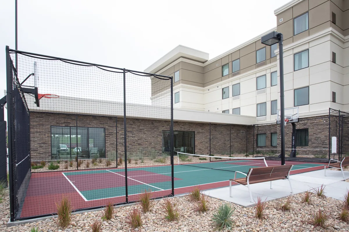 The image captures an inviting basketball court surrounded by manicured landscaping and comfortable benches. The setting suggests opportunities for active outdoor fun, friendly games, and socializing in a relaxed environment, perfect for families and groups.