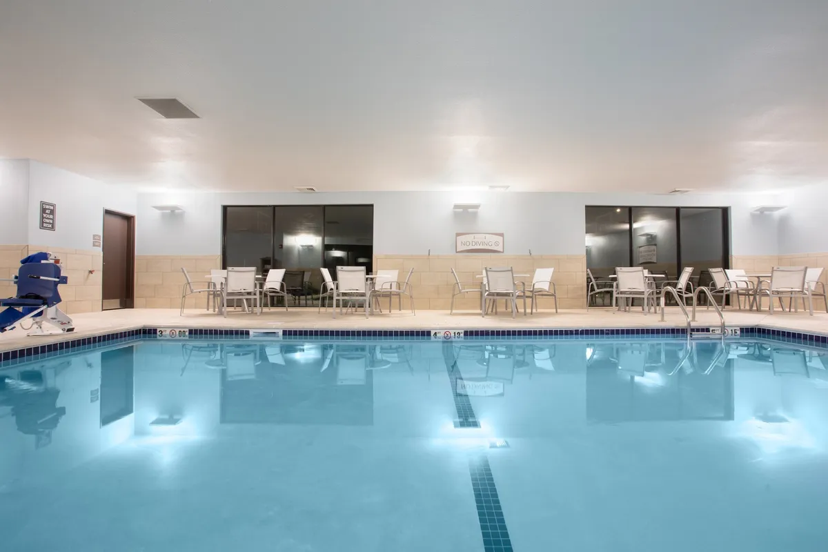 A tranquil indoor swimming pool with a comfortable seating area and large windows letting in natural light. The scene exudes relaxation, offering guests a calm place to unwind after work or energize with a swim.