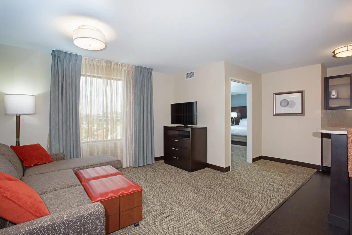 The image features a bright, inviting living area with a plush sofa facing a large television. Natural light pours in through a generous window, creating a cozy yet modern space perfect for relaxing or socializing. The setup suggests comfort and convenience, ideal for unwinding after exploring Denver.