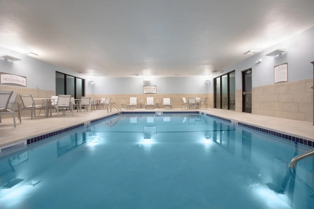 This image features a tranquil indoor swimming pool with a reflective water surface, complemented by lounge chairs arranged alongside the pool. The environment is serene, providing a sense of calm and relaxation. There is a subtle ambiance suggesting the possibility of both solitary relaxation and small group socialization.
