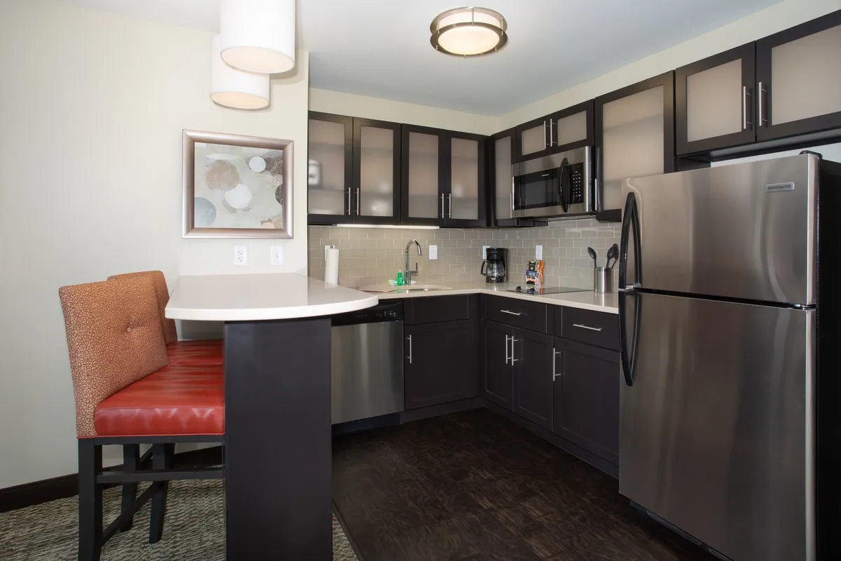 A bright, open-concept kitchen with stainless steel appliances, including a stove, microwave, and refrigerator. Bar seating invites casual dining or conversation, while framed artwork adds a homey touch. The space is tidy and thoughtfully arranged for both cooking and socializing.